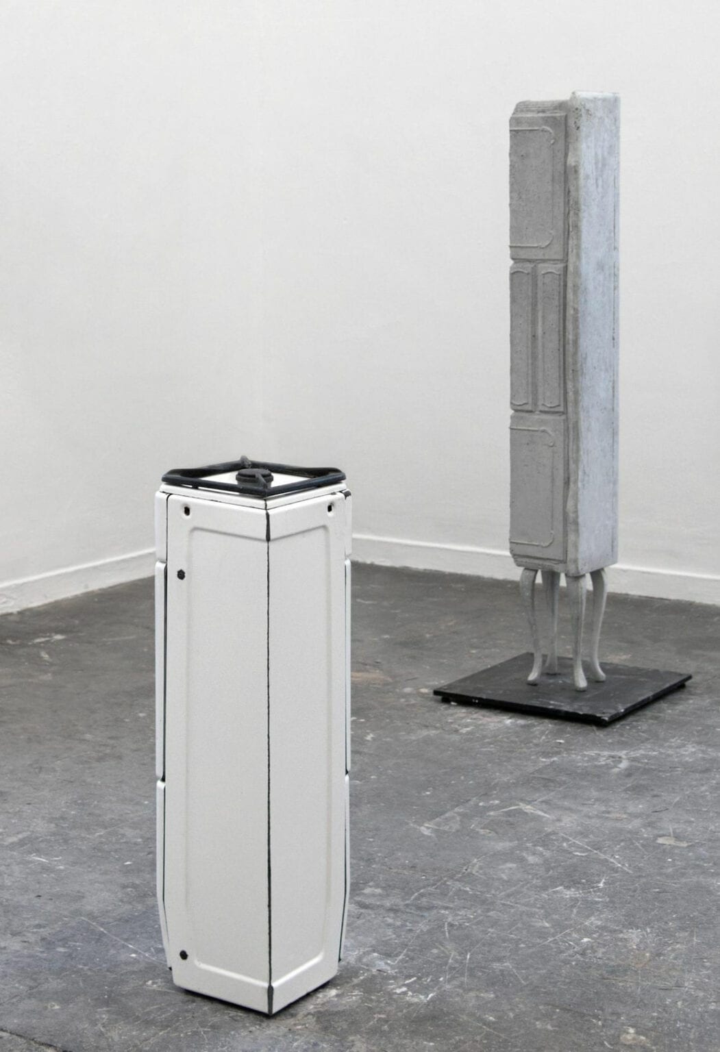 Foto: Ein Raum mit weißen Wänden und grauem, gefließten Steinboden. Im Raum stehen zwei große, längliche Skulpturen.