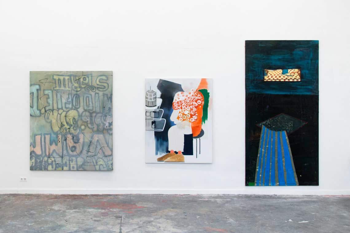 Foto: Ein Raum mit weißer Wand und grauem Boden. An der Wand hängen drei großformatige Leinwände.