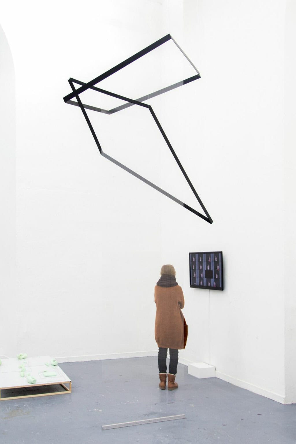 Foto: Ein Raum mit weißen Wänden und grauem Boden. Von der Decke hängt ein Objekt. An der Wand hängt ein Bildschirm. Auf dem Boden liegenden mehrere Objekte aus unterschiedlichen Materialien. Im Raum steht ein Mensch.