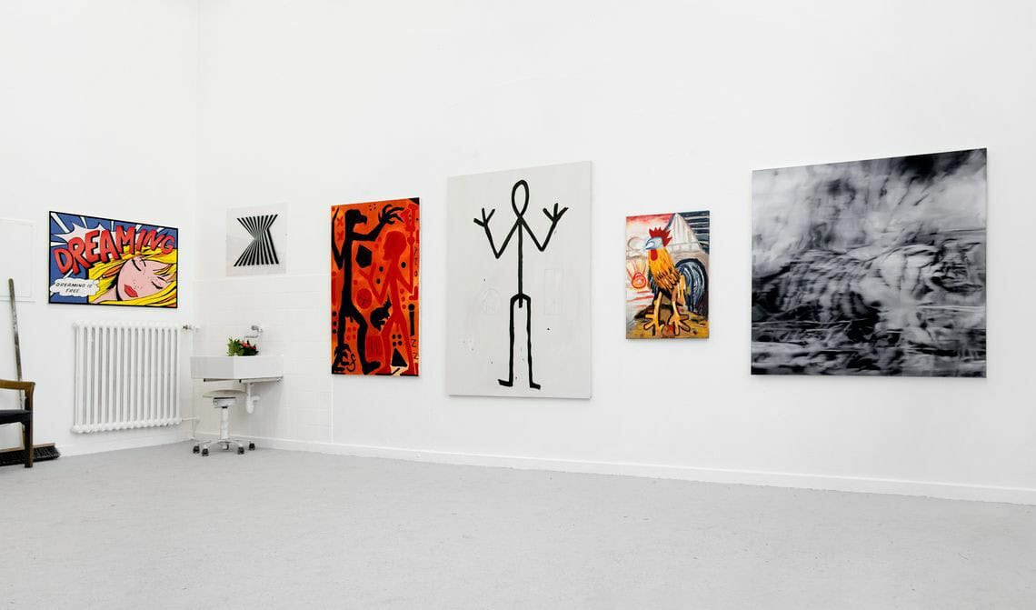 Foto: Ein Raum mit weißen Wänden und grauem Boden. An den Wänden hängen, auf ähnlicher Höhe nebeneinander, mehrere Leinwände in Mittel- und Großformaten.