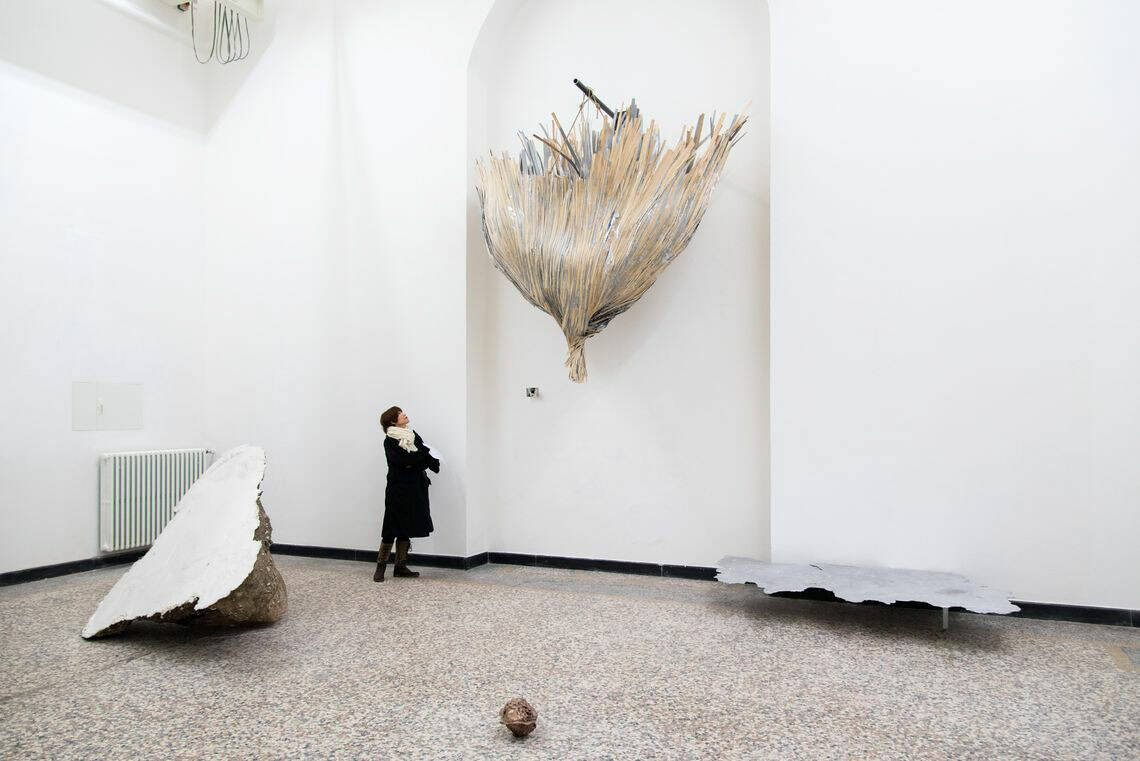 Foto: Ein Raum mit weißen Wänden, mehrfarbigem Steinboden und einer wandhohen, bogenförmigen Einbuchtung. In der Einbuchtung und auf dem Boden befinden sich mehrere große Objekte.