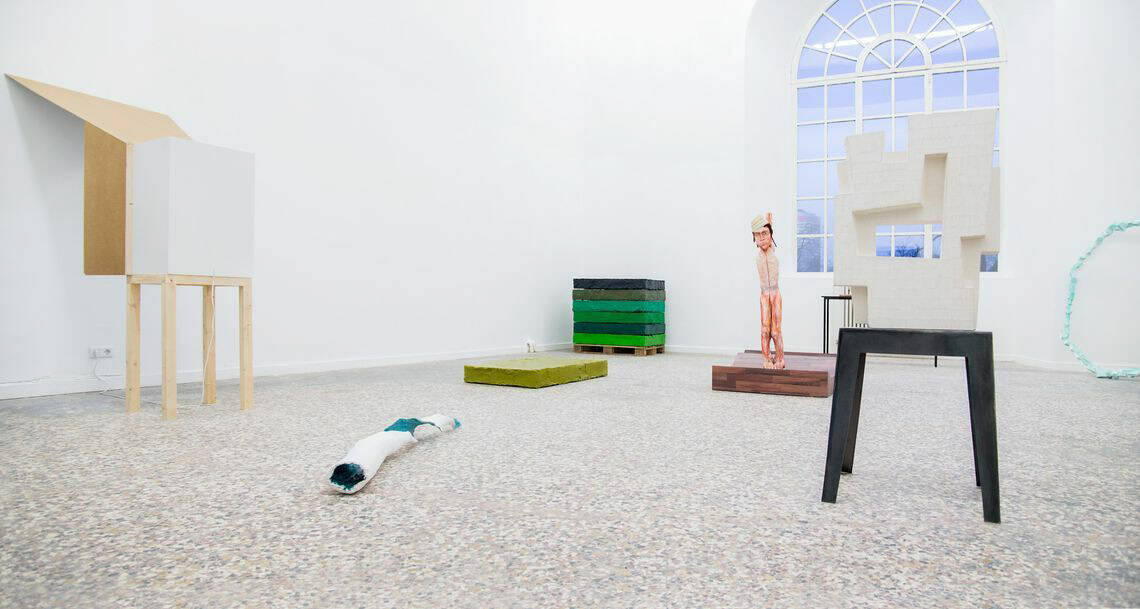 Foto: Ein Raum mit weißen Wänden, mehrfarbigem Steinboden und einem großen Fenster. Im Raum befinden sich mehrere Skulpturen aus unterschiedlichen Materialien.