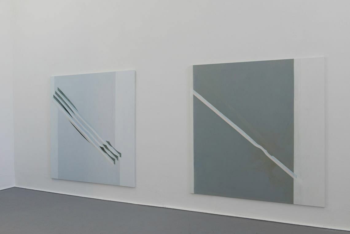 Foto: Ein Raum mit weißen Wänden und grauem Boden. An der Wand hängen zwei Leinwände im ähnlichen Format, auf gleicher Höhe.