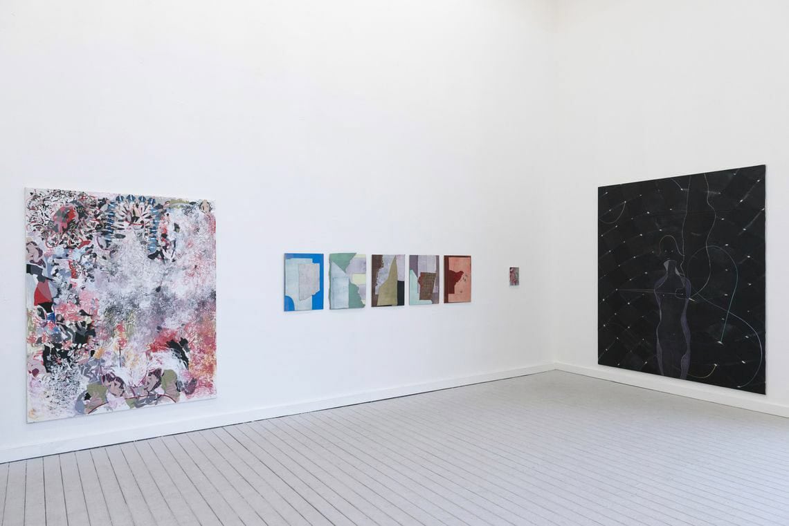 Foto: Ein Raum mit weißen Wänden und grauem Dielenboden. An der Wand befinden sich zwei großformatige Leinwände und eine auf gleicher Höhe hängende Reihe aus klein- und mittelformatigen, flachen Objekten.