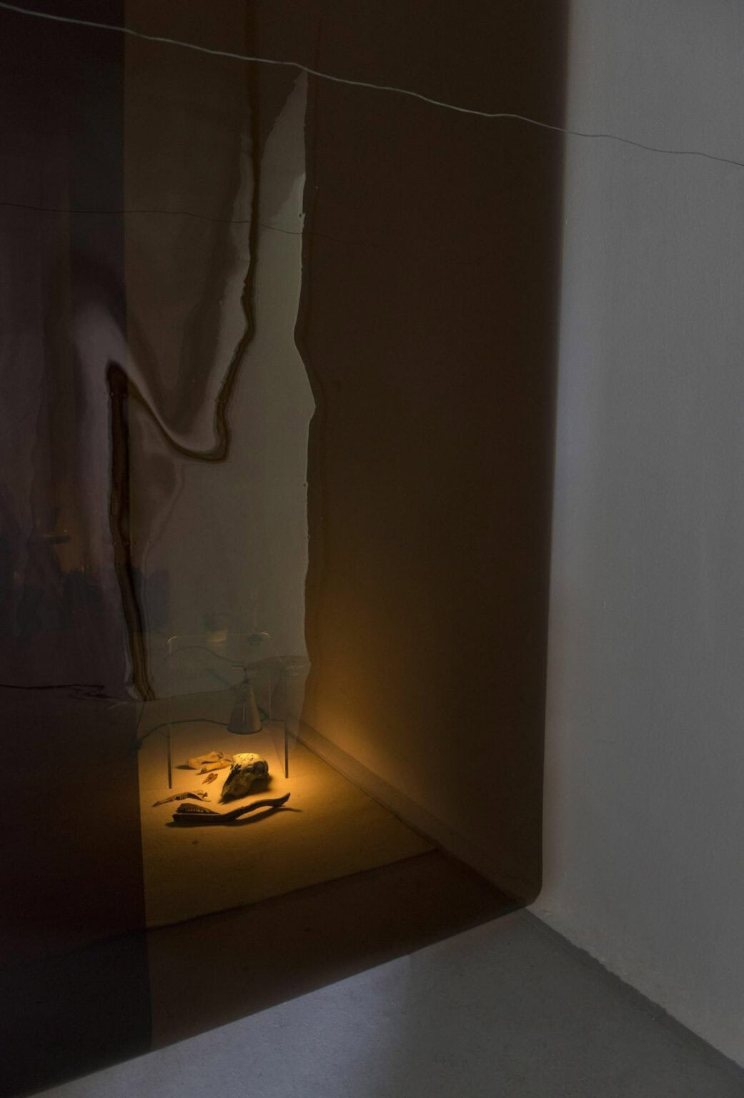 Foto: Ein Raum mit einem schmalen, abgedunkelten Areal. In dem Areal befinden sich Objekte, die von einem warmen Licht anstrahlt werden.