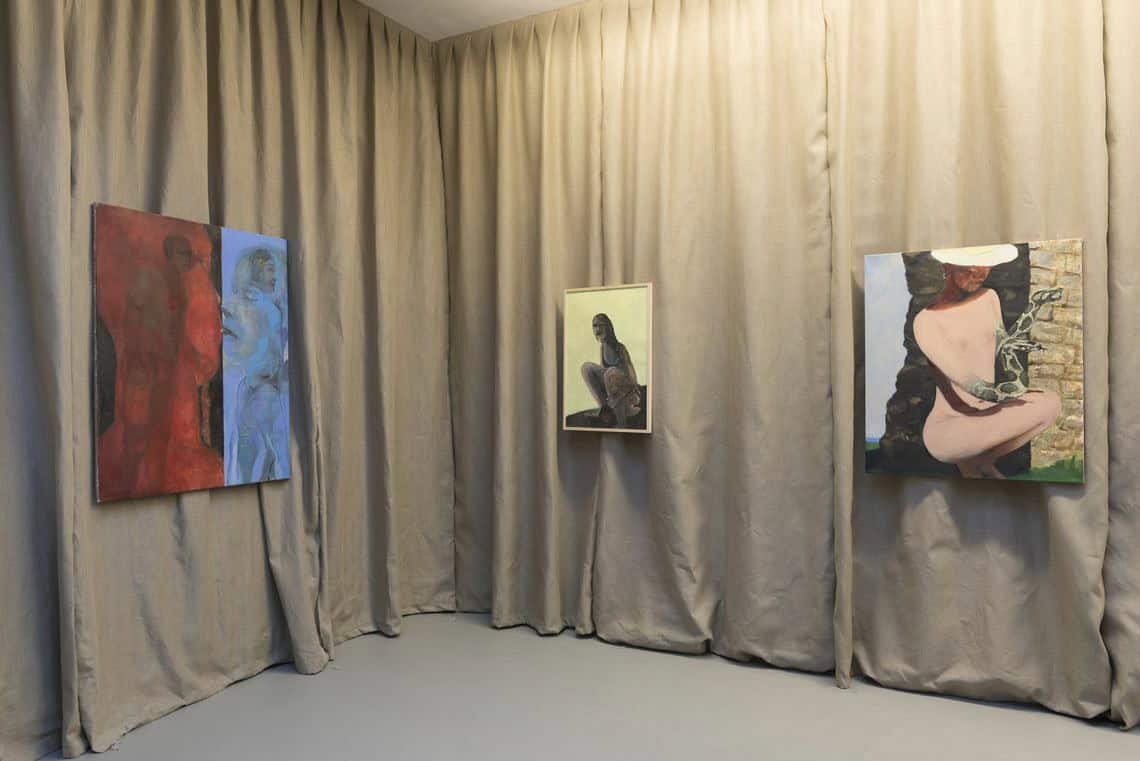 Foto: Eine Wand aus beigen Vorhängen. Auf dem Vorhang sind gerahmte und ungerahmte Leinwände in Mittelformaten angebracht.