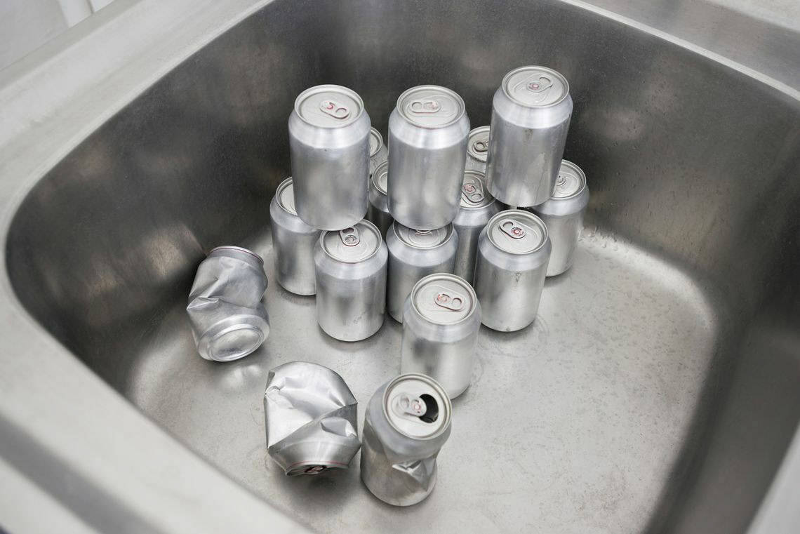 Foto: Ein Waschbecken auf Metall. Innerhalb des Beckens befindet sich mehrere Silberfarbene Dosen, die auf- und nebeneinander stehen. Manche von ihnen sind geöffnet und zerdrückt, andere sind unversehrt und geschlossen.