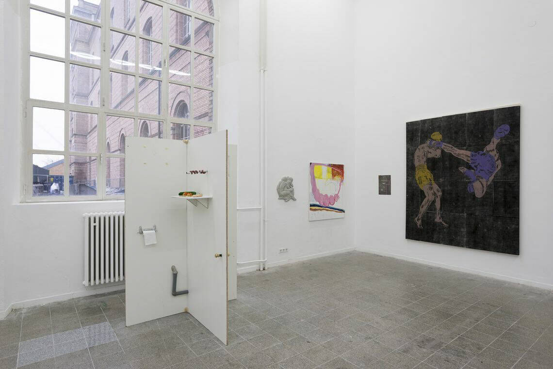 Foto: Ein Raum mit weißen Wänden, grauem, gefließten Boden und einem großen Fenster. An den Wänden des Raumes befinden sich mehrere flache Objekte . Im räum steht eine verwinkelte Konstruktion aus unterschiedlichen Materialien.