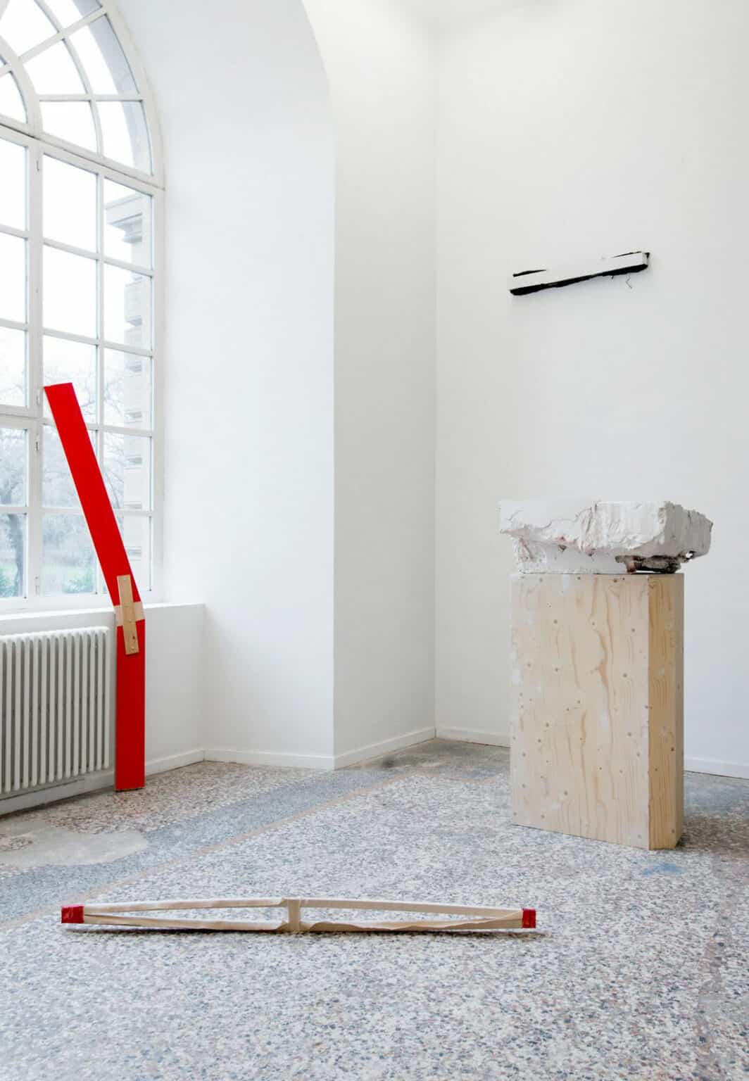 Foto: Ein Raum mit weißen Wänden, mehrfarbigem Steinboden und einem großen Fenster. m Raum befinden sich mehrere große Skulpturen auf unterschiedlichen Materialien. Manche von ihnen liegen auf dem Boden, andere lehnen an der Wand und dem Fenster oder stehen auf Sockeln.